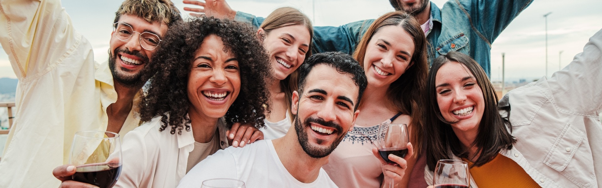 Group of young adult best friends having fun toasting a red wine glasses at rooftop reunion or birthday party, drinking alcohol. Happy people enjoying on a social gathering celebrating together. High