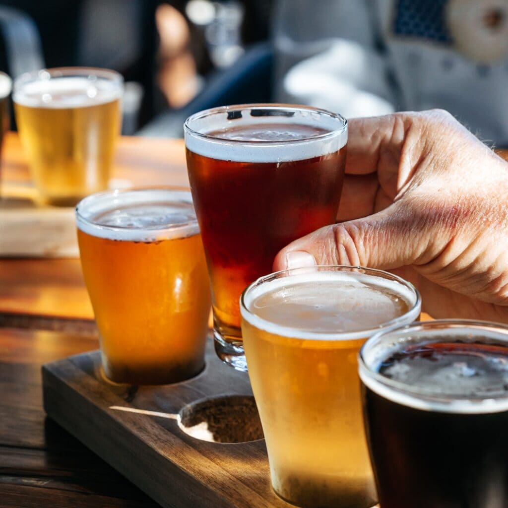 Hand lifting a glass of beer from a tasting paddle in Perth, Western Australia