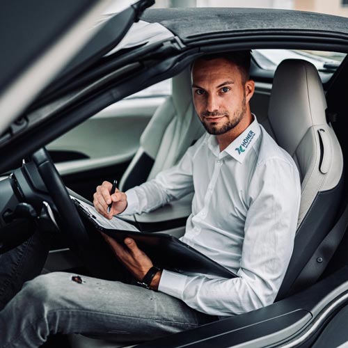 Mann in weißem Hemd im Auto, ernst blickend, schreibt auf Klemmbrett.