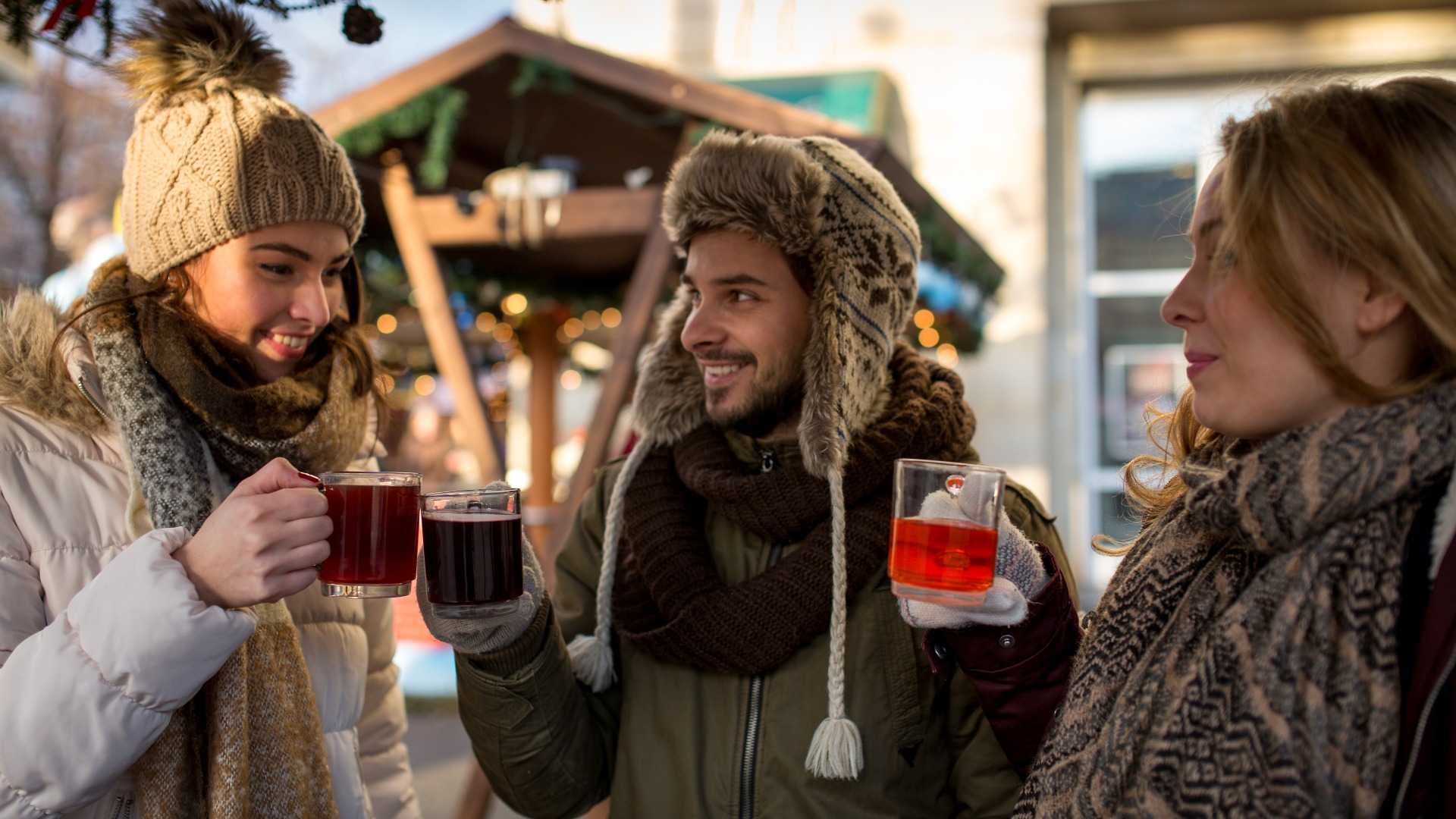 Ehepaar und Freund, Freunde auf einem deutschen Weihnachtsmarkt, die den traditionellen Glühwein genießen und miteinander reden
