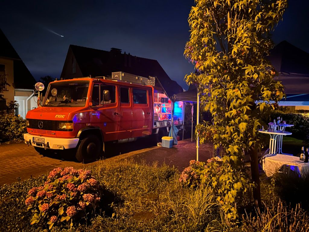 Ein rotes Feuerwehrauto steht nachts beleuchtet in einer Einfahrt neben einem Baum