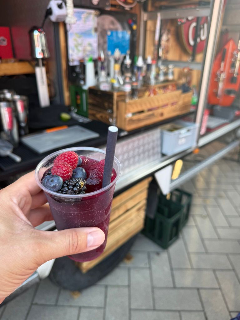Eine Hand hält ein lila Getränk mit Eis und frischen Beeren vor einer Bar